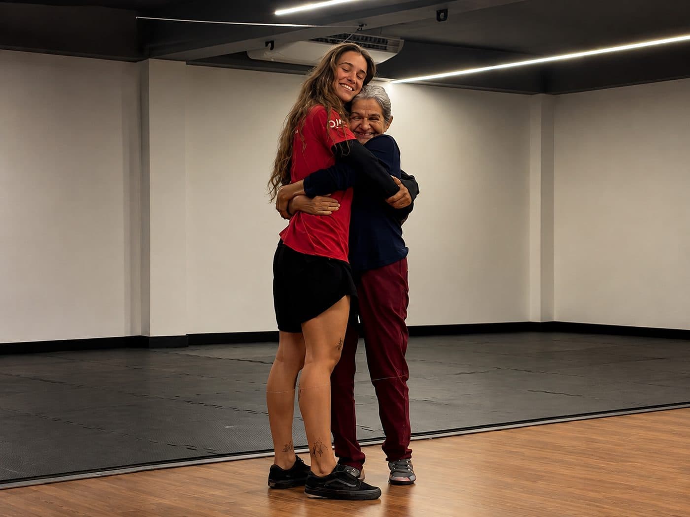 Layla Soares abraçada com uma aluna de cabelos grisalhos, as duas sorrindo, ao fim de um treino